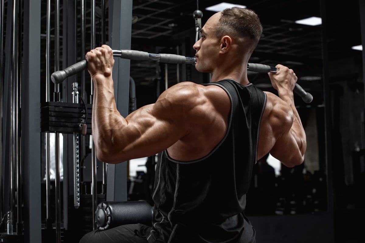 Muscular man workout in gym, doing exercise for back lat pulldown. Strong male rear view